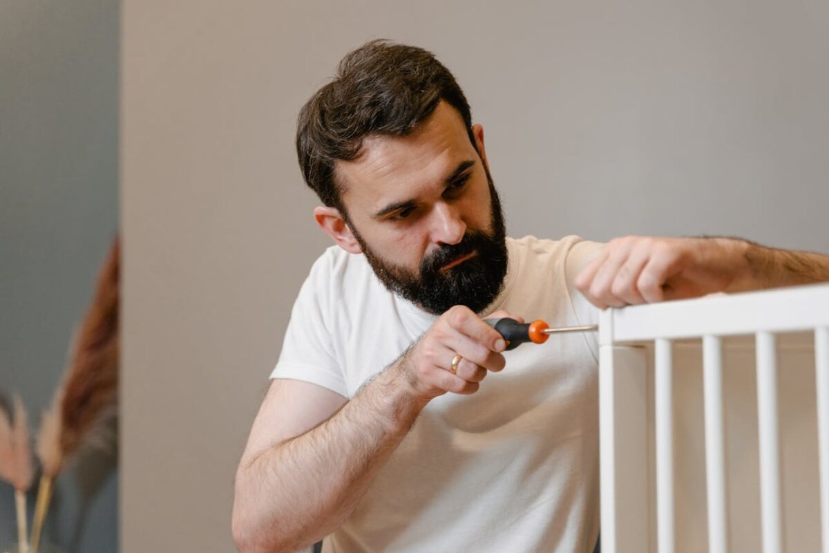 services-02 A man focusing closely on assembling a baby crib with a screwdriver in a well-lit room.
